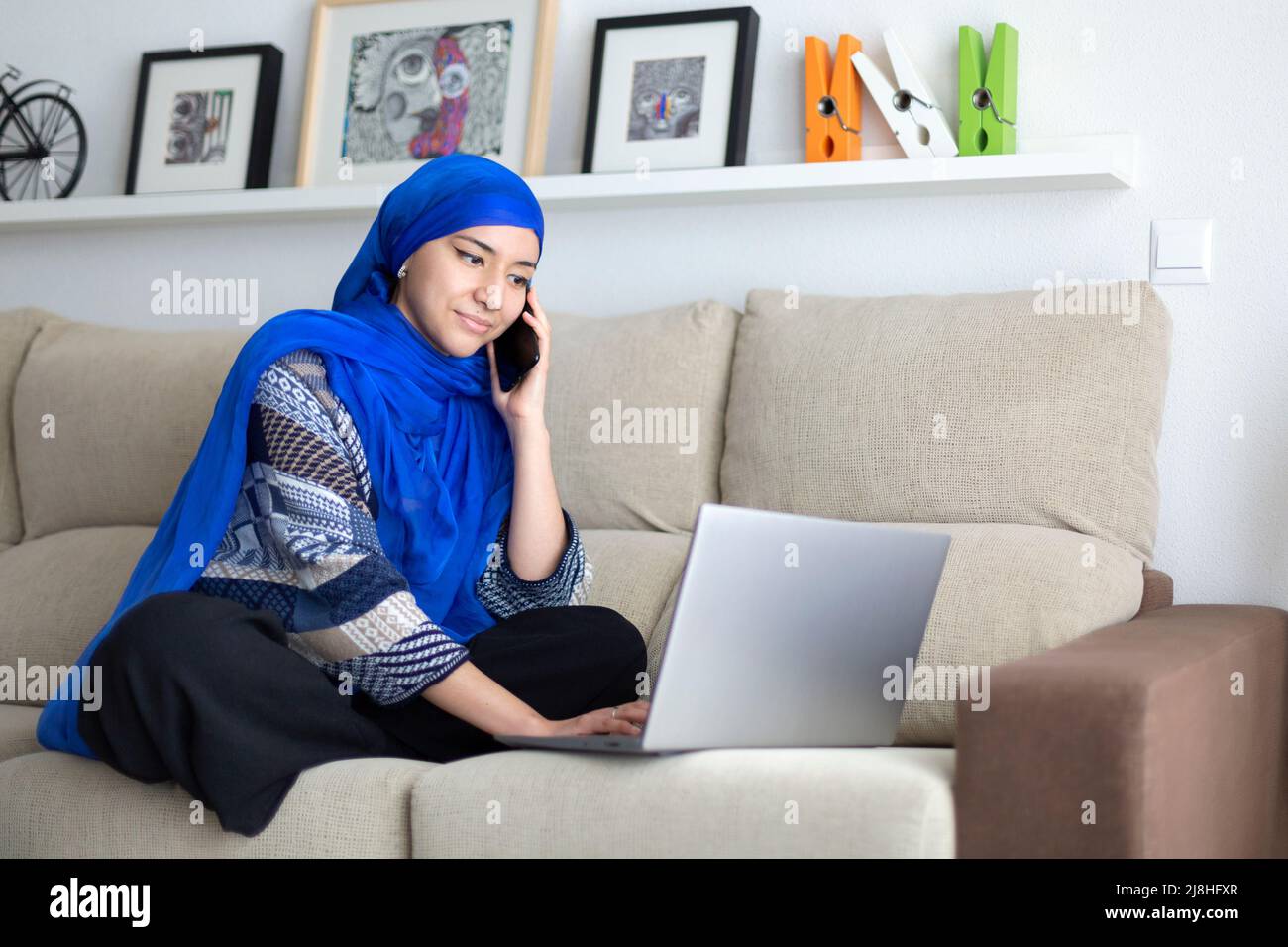 Jeune femme musulmane utilisant un ordinateur portable dans le salon. Travailler à domicile. Espace pour le texte. Banque D'Images