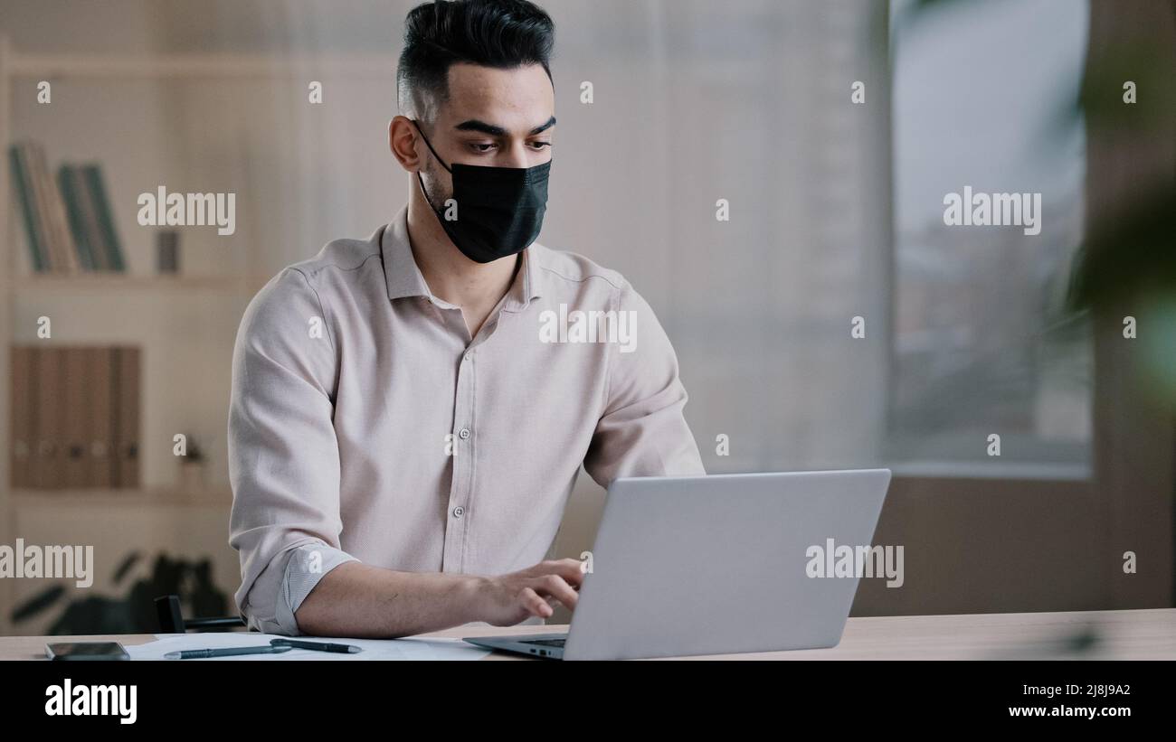 Hispanique arabe homme d'affaires homme masqué travailleur programmeur dactylographiant sur ordinateur portable recherche d'informations en ligne dans le cyberespace développement de projet d'entreprise utilisant Banque D'Images