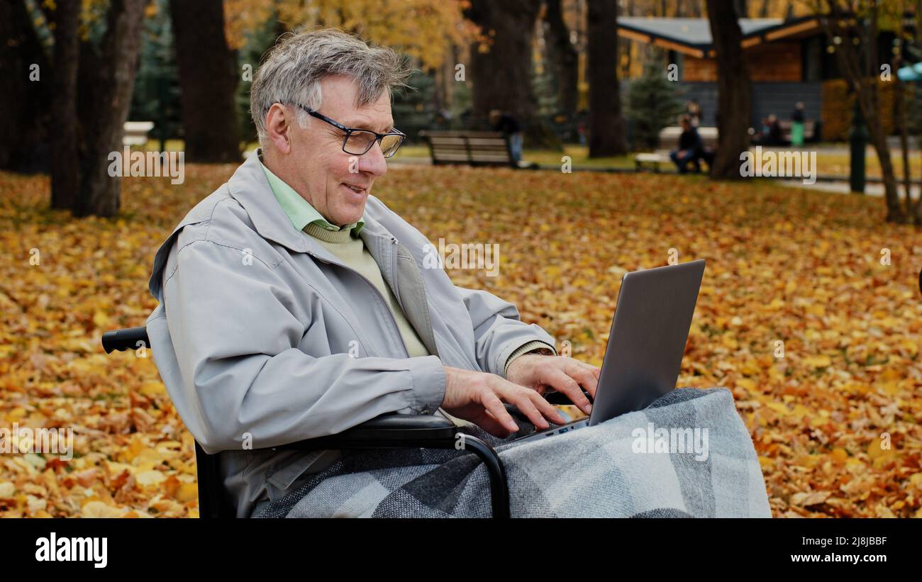 Heureux senior caucasien ancien homme vieux retraité grand-père assis seul sur fauteuil roulant mature gris-cheveux retraité homme solitaire travail sur ordinateur portable gagner en ligne Banque D'Images