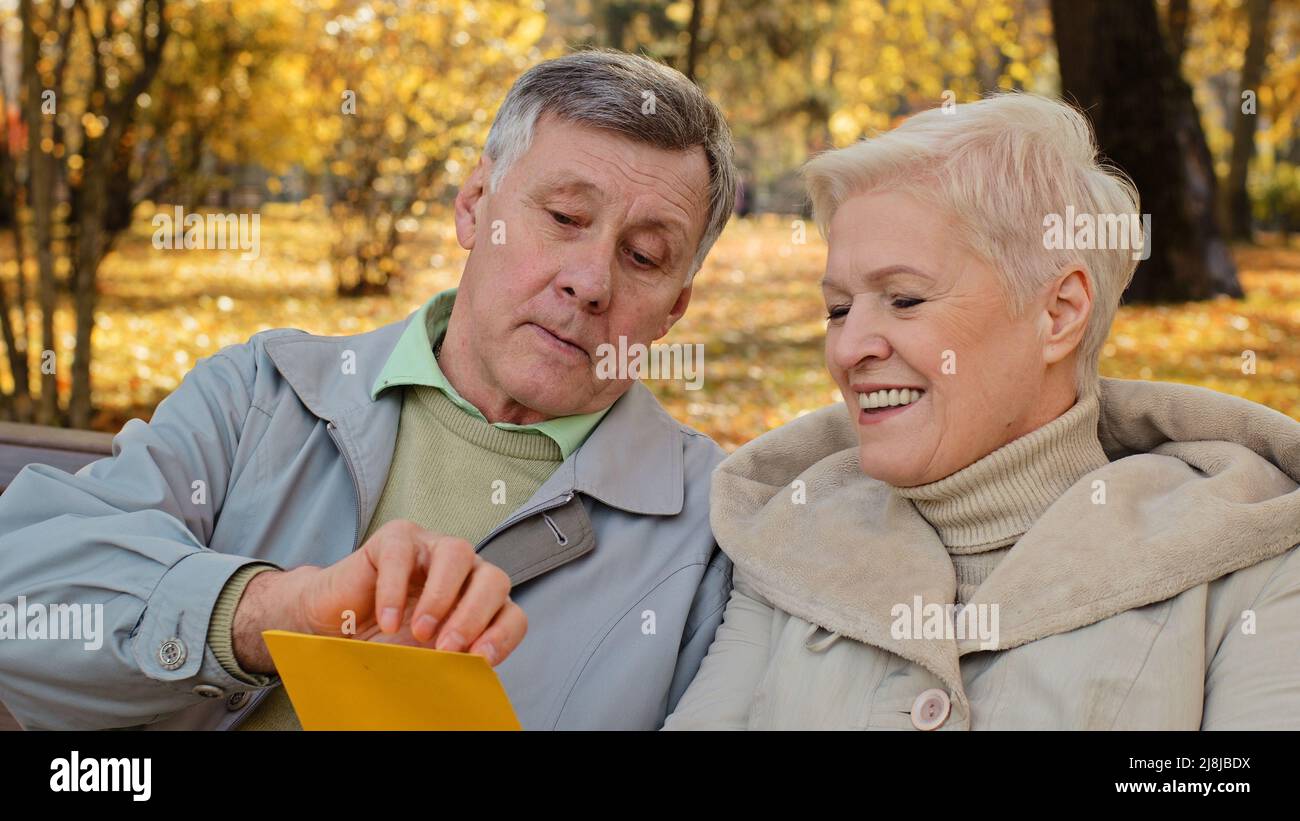 Souriant couple âgé partenaires grands-parents femme principale mari ouvrir l'enveloppe postale entrante lit les bonnes nouvelles lettre banque prêt papier Banque D'Images