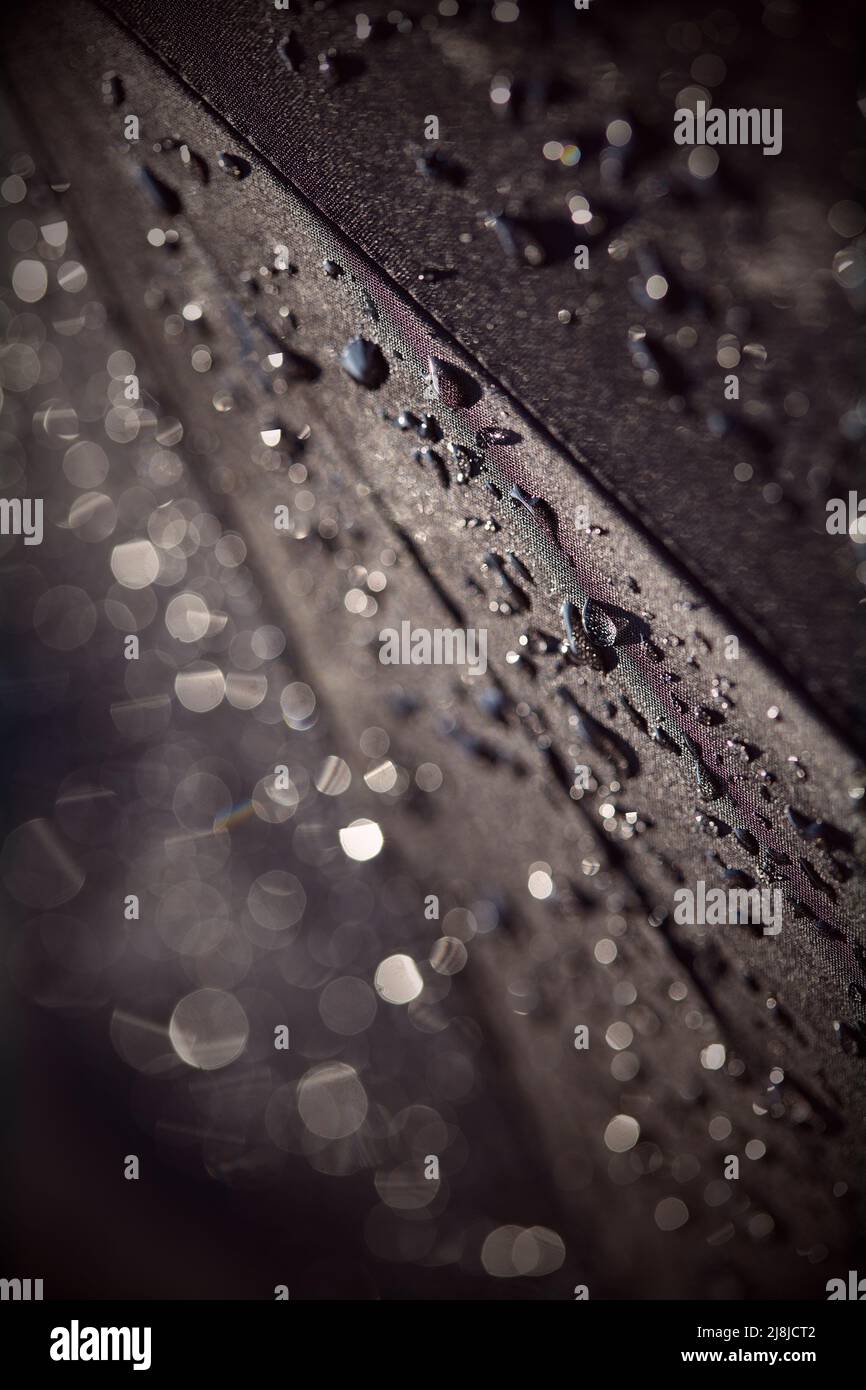 Arrière-plan noir abstrait avec une teinte bordeaux. Gouttes de pluie floues avec bokeh sur un parapluie noir. Gouttes d'eau de pluie sur un tissu noir imperméable. RA Banque D'Images