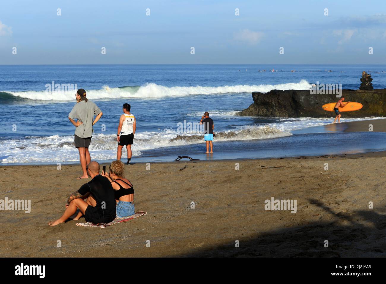 Plusieurs personnes, dont plusieurs Caucasiens assis et debout à Batu Bolong Beach à Canggu, Bali, Indonésie regardant le surfeur dans l'océan. Banque D'Images
