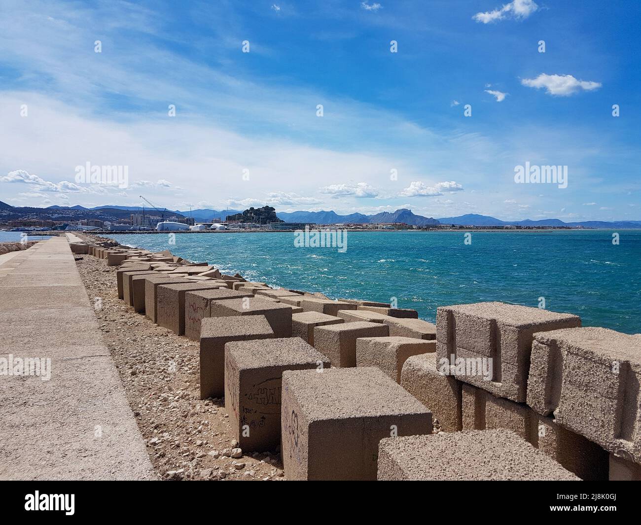 Blocs rectangulaires sur le mur du port de Denia surplombant la mer en face du port sous le ciel bleu ensoleillé, légèrement nuageux Banque D'Images