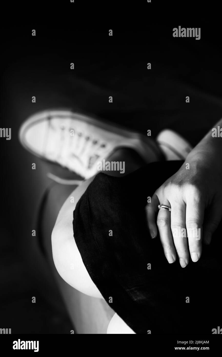 Une photo en noir et blanc d'une femme assise, des mains dans le cadre et des pieds. Photo verticale. Banque D'Images