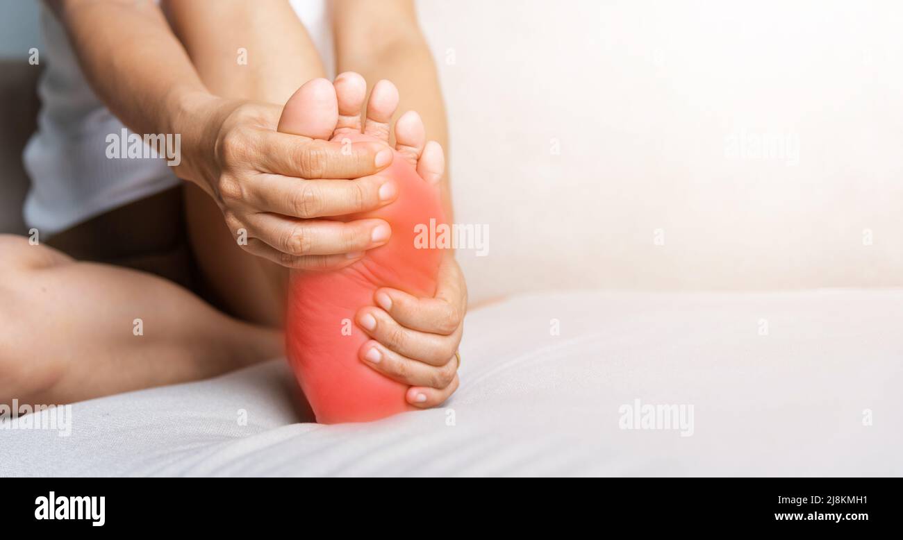 Douleur de pied, femme asiatique assise sur un canapé sentant la douleur dans son pied à la maison, femme souffrant de douleur de pieds utilisation massage de main détendre muscle de la plante en h Banque D'Images