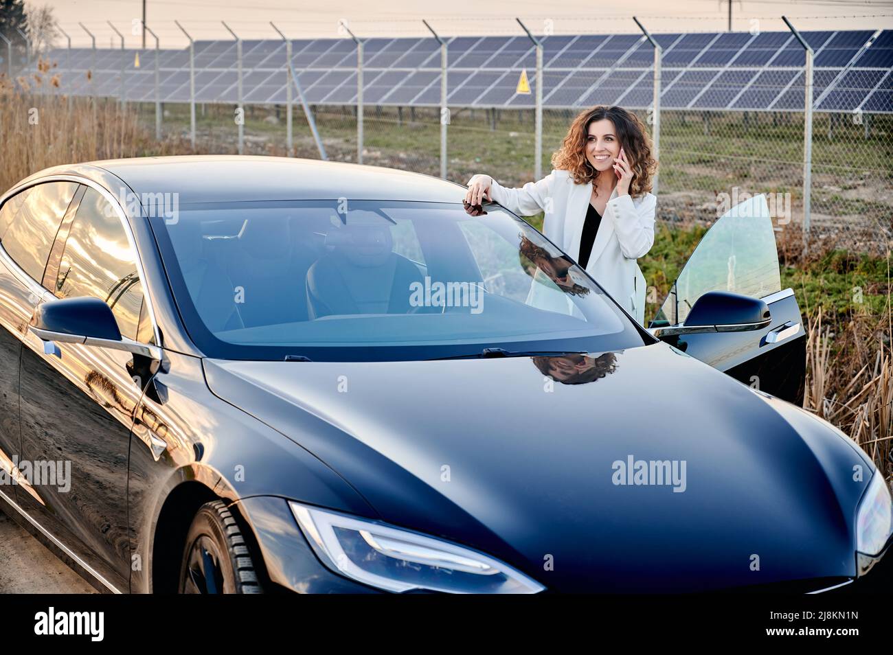 Jeune femme parlant au téléphone en se tenant près d'une voiture ouverte. Sur la centrale solaire backdrop produisant de l'électricité durable et des énergies renouvelables. Économie et écologie énergie indentisterie. Banque D'Images