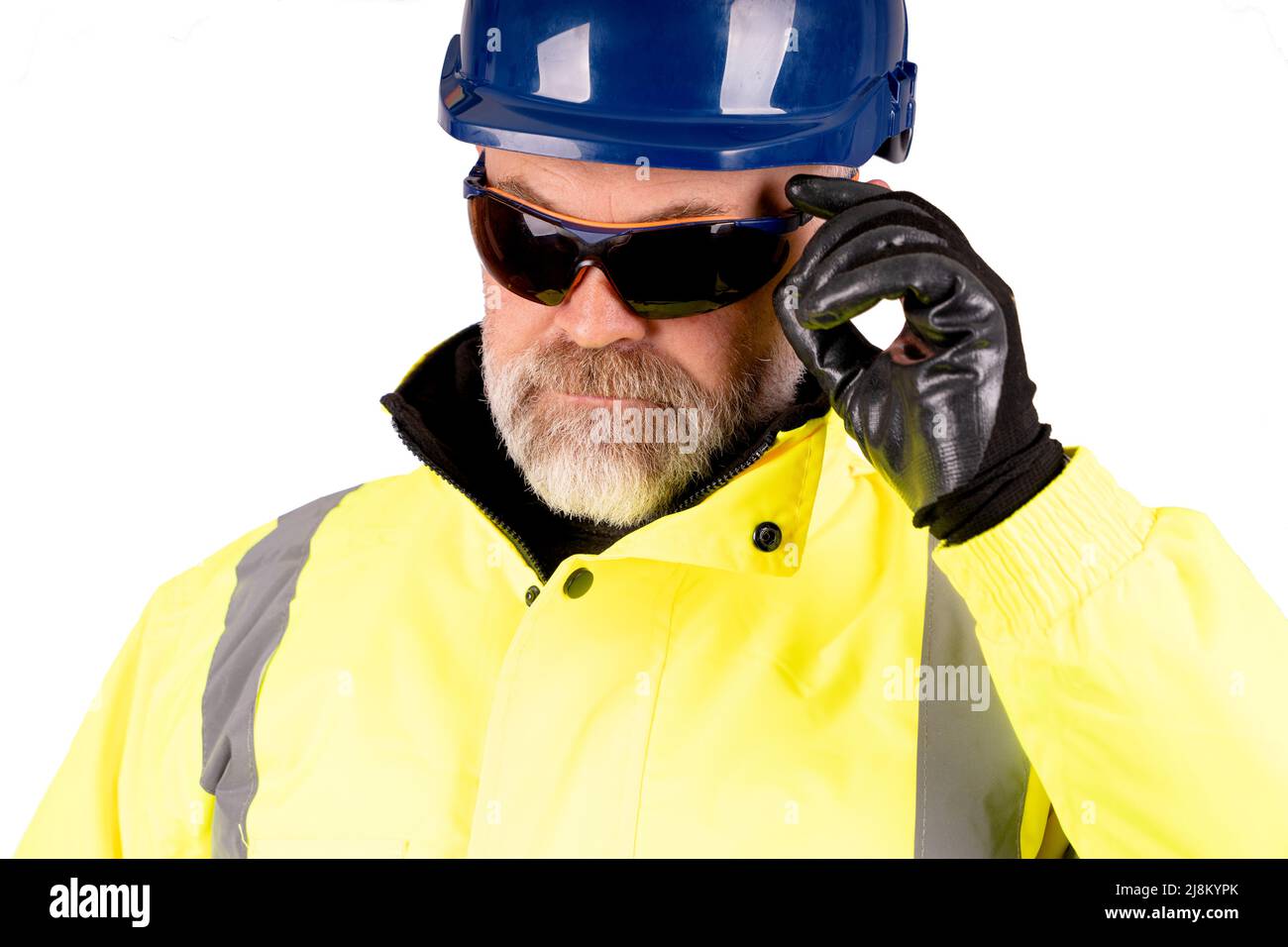 Un ouvrier de la construction, vêtu d'un chapeau bleu et d'un manteau jaune de haute viz sur fond blanc, portant des lunettes de sécurité teintées foncé Banque D'Images