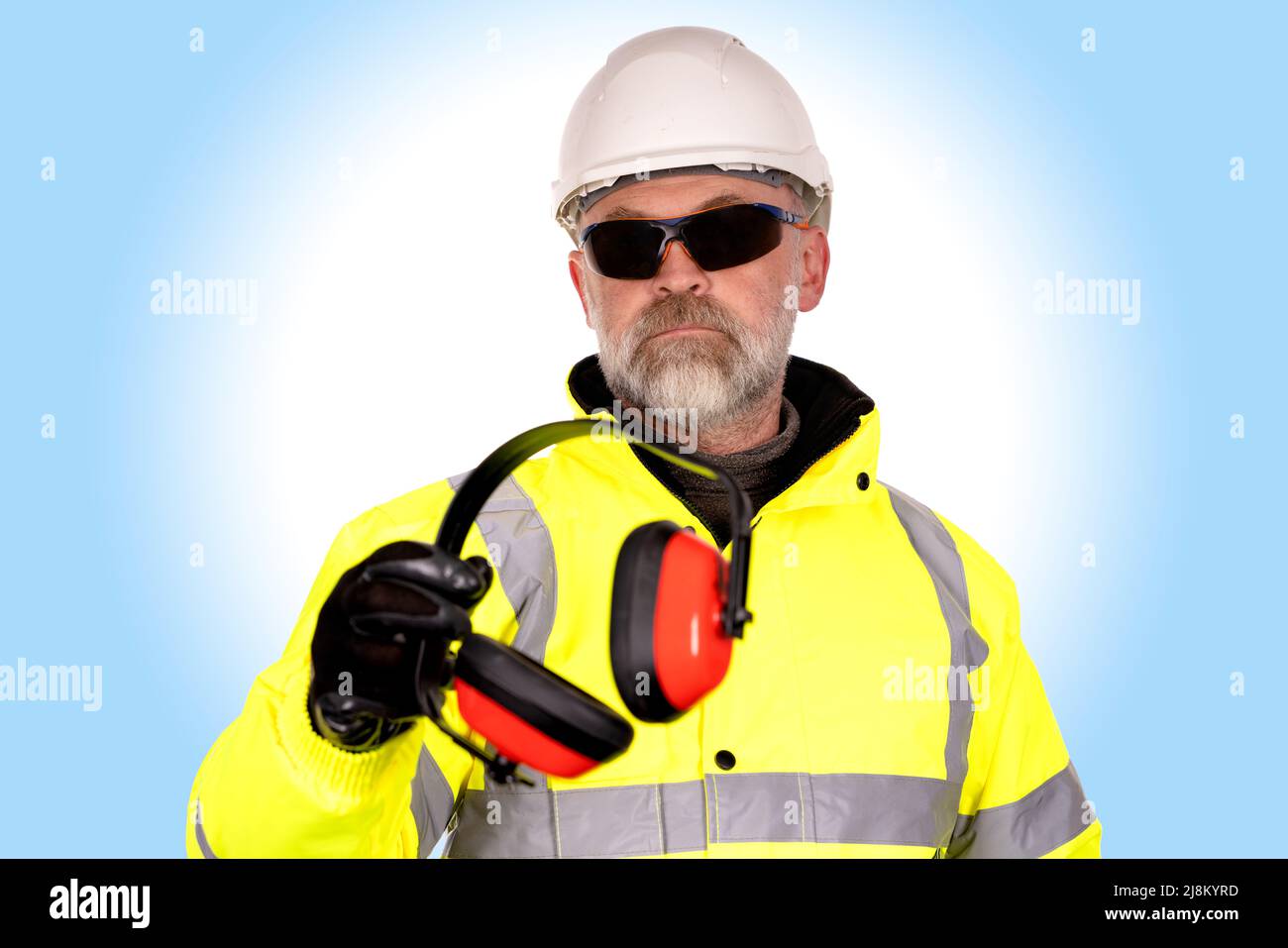 Un ouvrier de la construction dans un chapeau blanc, un manteau jaune de haute viz et des lunettes de sécurité teintées foncé sur le fond bleu clair donne la mousse-rempli d'oreille def Banque D'Images