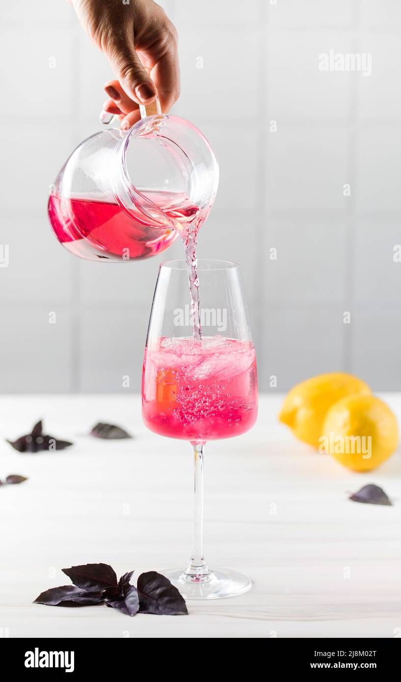 La main d'une femme verse une limonade au basilic rouge rafraîchissante dans un verre à partir d'une verseuse. Boissons d'été. Banque D'Images