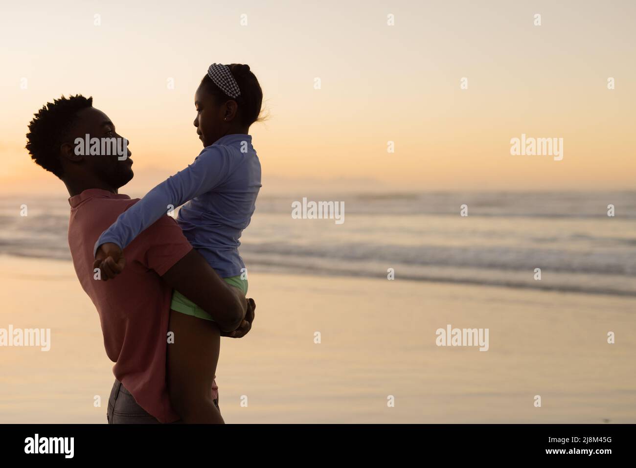 Jeune homme afro-américain qui prend sa fille en se tenant contre la mer et en admirant le ciel au coucher du soleil Banque D'Images