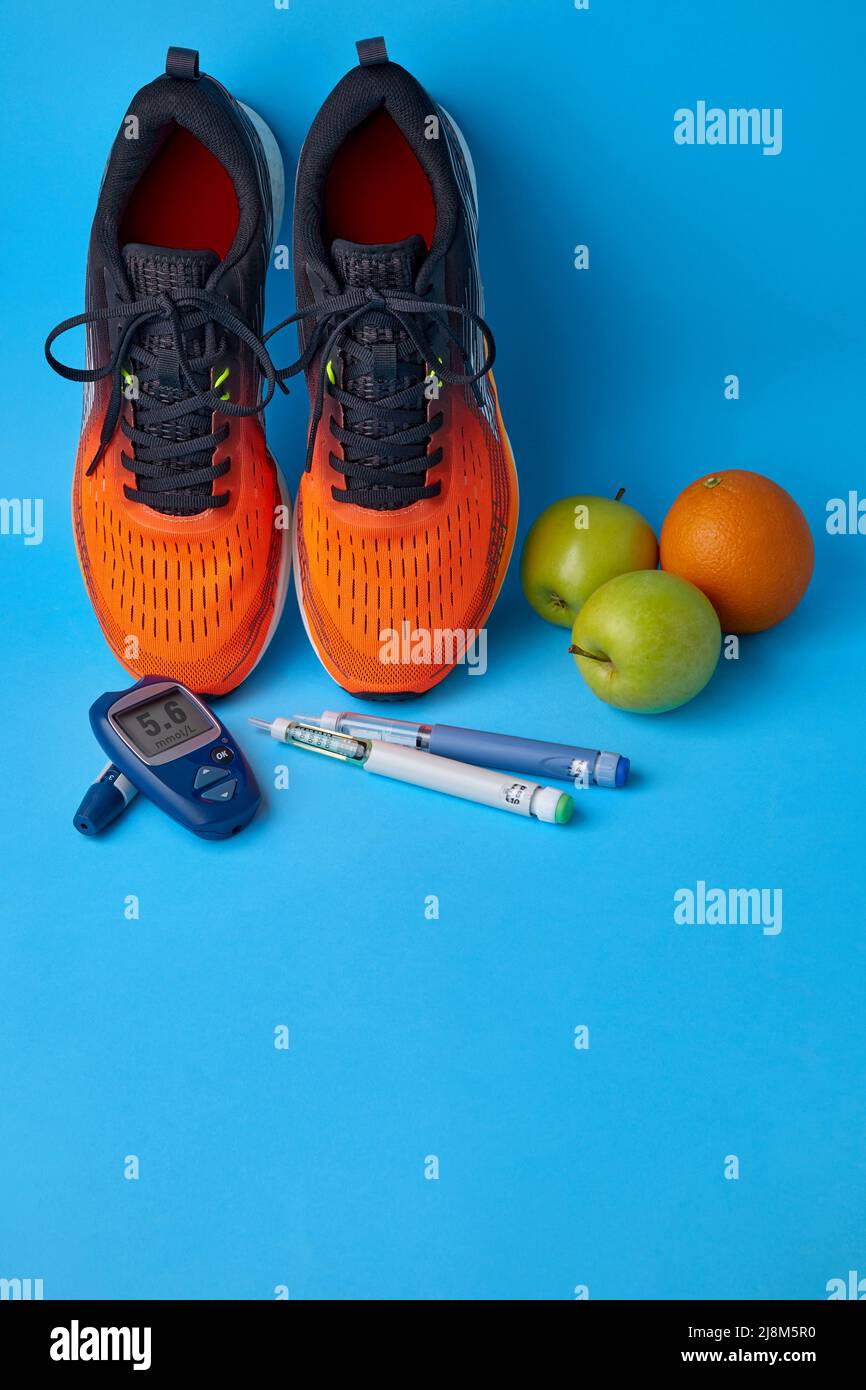 Baskets orange, pommes vertes, oranges, glucomètre et stylos à seringue d'insuline sur fond bleu avec espace de copie. Traitement de la résistance à l'insuline et d Banque D'Images