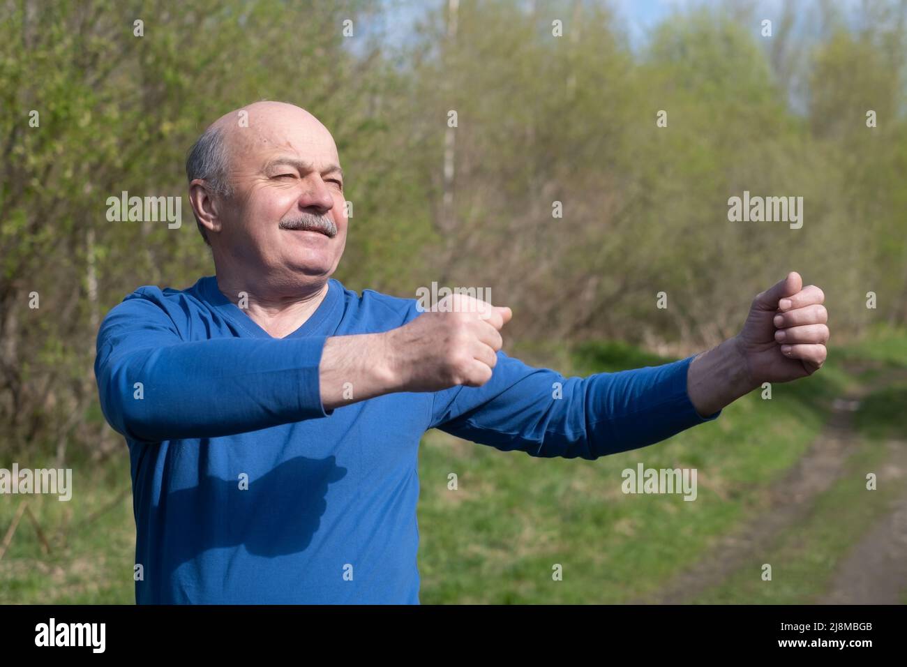 Coureur senior avec brassard s'étirant. Nature printanière. Un mode de vie sain à la vieillesse. Banque D'Images