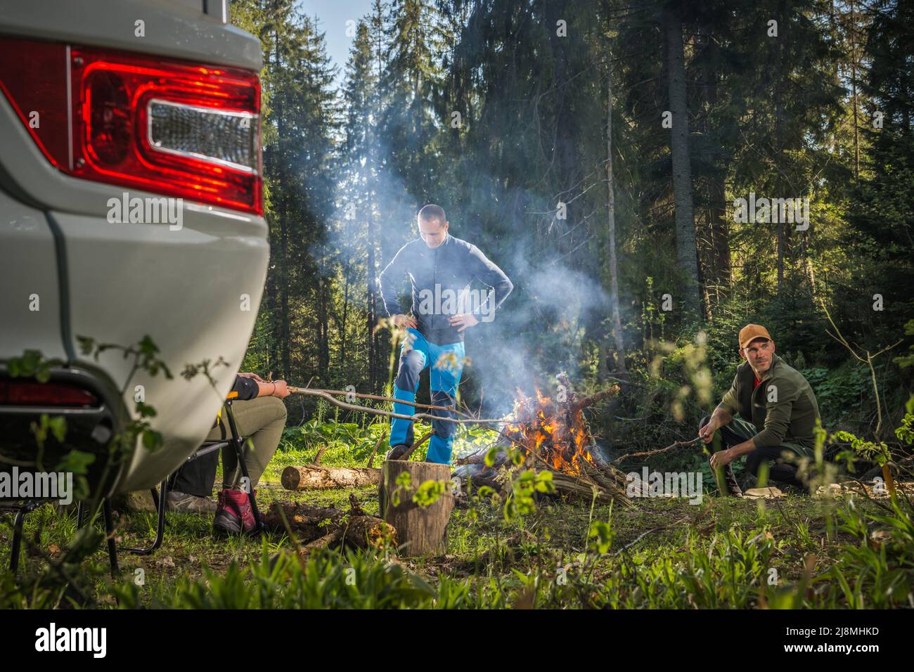 Les amis du Caucase dans leur 40s pendent à côté de Campfire et de camping-car Van dans la nature pittoresque de Woodland Wilderness. Terrain de camping sec pour véhicules de plaisance. Banque D'Images