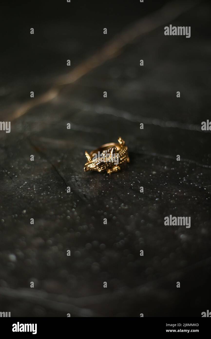 Bague dorée en forme de crocodile sur fond de marbre foncé Banque D'Images