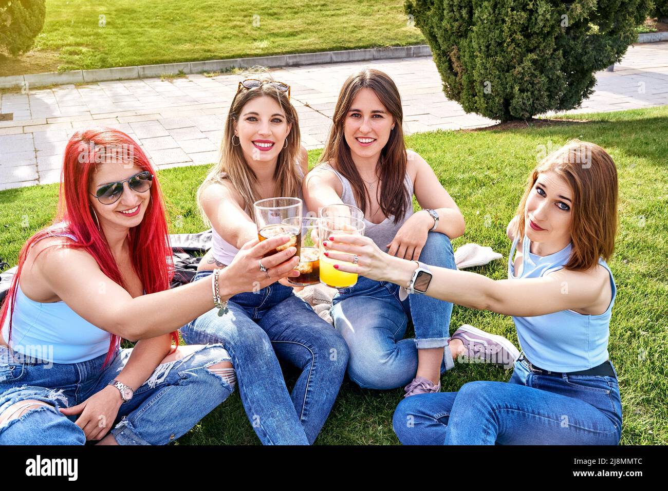 Quatre amis assis sur l'herbe, prenant des boissons et des toasts tout en regardant l'appareil photo un jour ensoleillé. Photo de haute qualité Banque D'Images