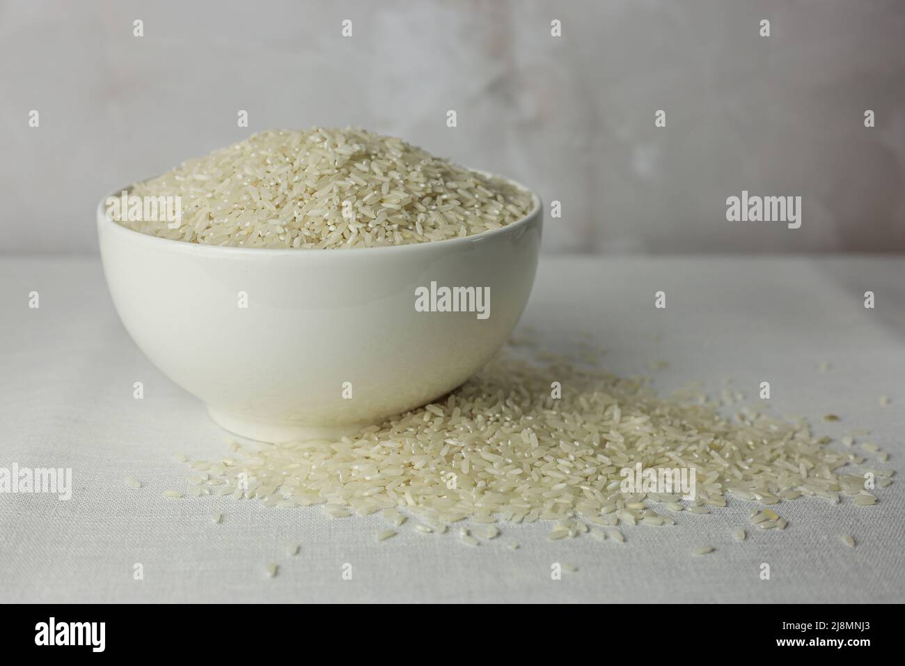 Riz dans un plat blanc profond vue rapprochée sur un tissu blanc texturé Banque D'Images