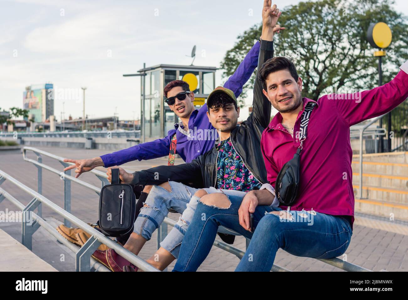 trois amis de sexe masculin gay de race blanche, portant des vêtements décontractés, assis sur un garde-corps à l'extérieur, heureux de regarder l'appareil photo, concept de style de vie, espace de copie. Banque D'Images