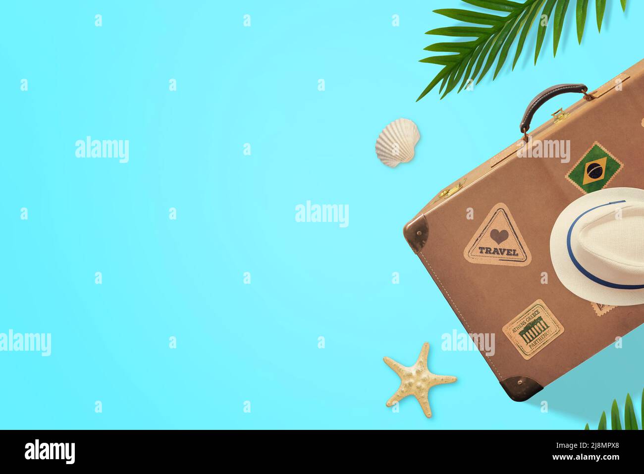 Valise rétro et chapeau sur une surface bleue avec des feuilles de palmier à côté. Vue de dessus, composition de la pose à plat avec espace de copie Banque D'Images