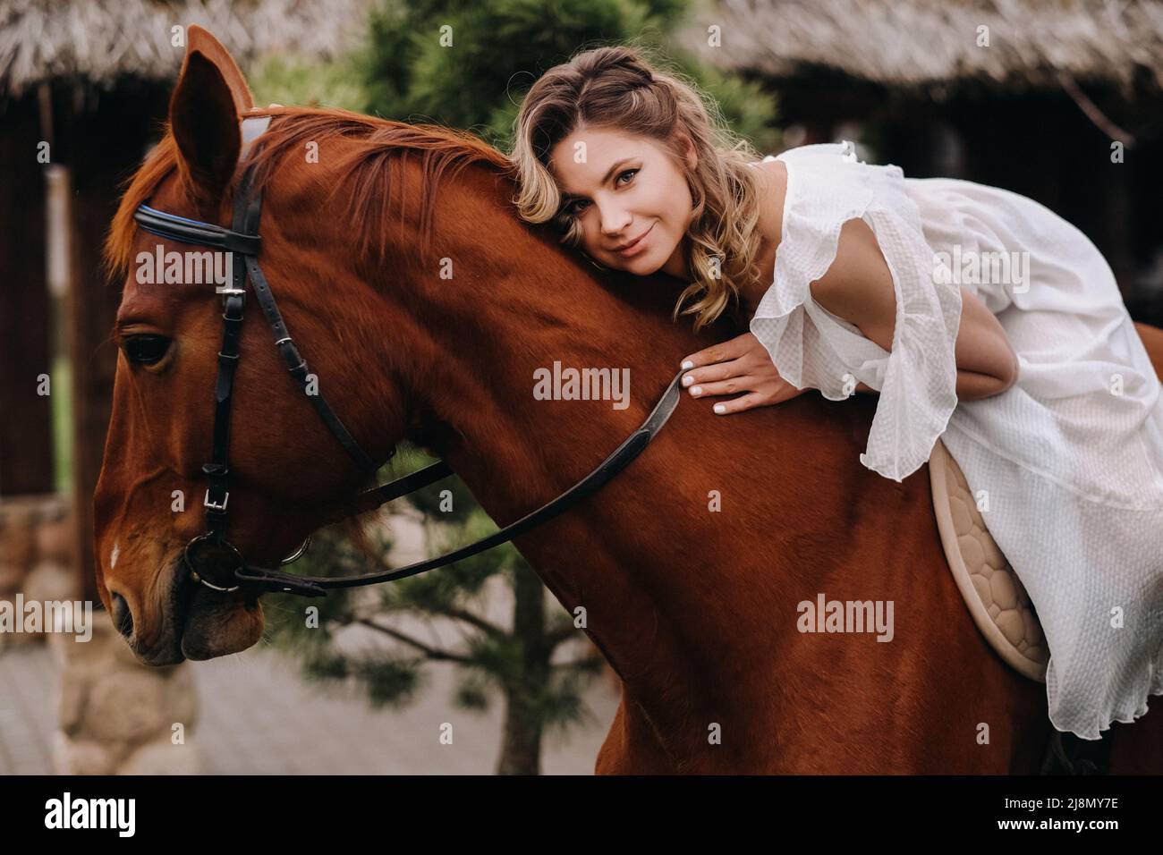 Une femme dans une sundress blanche à cheval près d'une ferme Banque D'Images