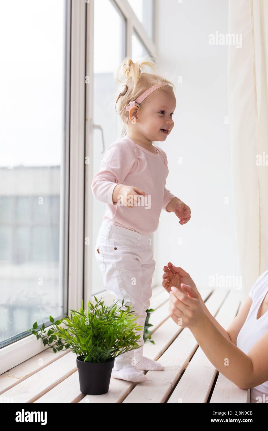 Implant cochléaire pour bébé. Un enfant sourd avec prothèse auditive joue dans le salon Banque D'Images