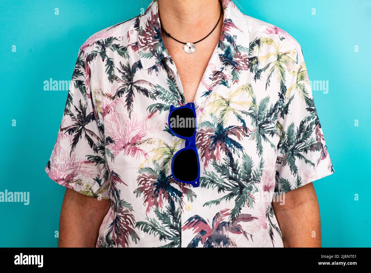 Gros plan de lunettes de soleil bleues suspendues à une chemise hawaïenne avec fond vert. Banque D'Images