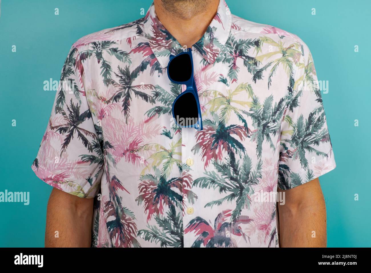 Gros plan de lunettes de soleil bleues suspendues à une chemise hawaïenne avec fond vert. Banque D'Images