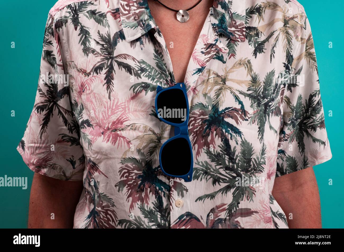 Gros plan de lunettes de soleil bleues suspendues à une chemise hawaïenne avec fond vert. Banque D'Images