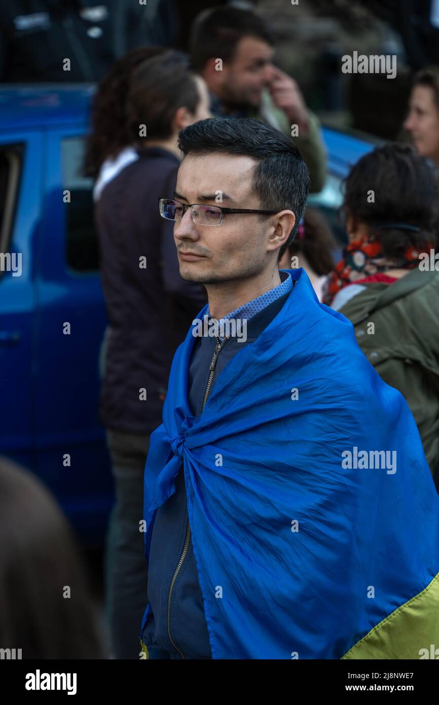 Sofia, Bulgarie - 09 mai 2022: Un jeune homme, portant des lunettes et enveloppé dans le drapeau ukrainien marche dans une foule Banque D'Images