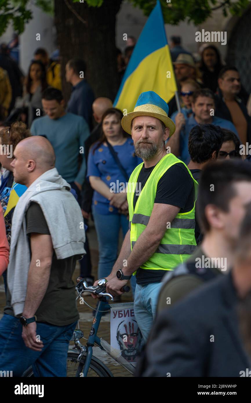 Sofia, Bulgarie - 09 mai 2022 : un homme, vêtu d'un gilet de visibilité jaune et d'un chapeau bleu-jaune, tient dans une foule, tenant son bycicle, avec un Ukranian f Banque D'Images