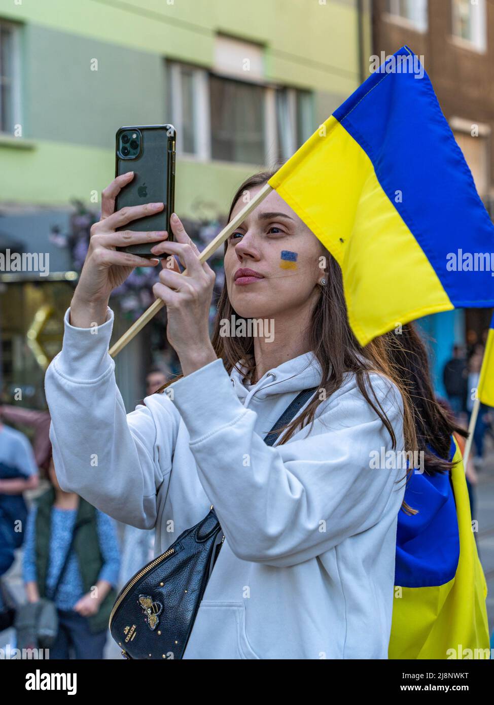 Une jeune femme avec un drapeau ukrainien de taille moyenne, élevée dans sa main, tire la démonstration sur son smartphone Banque D'Images