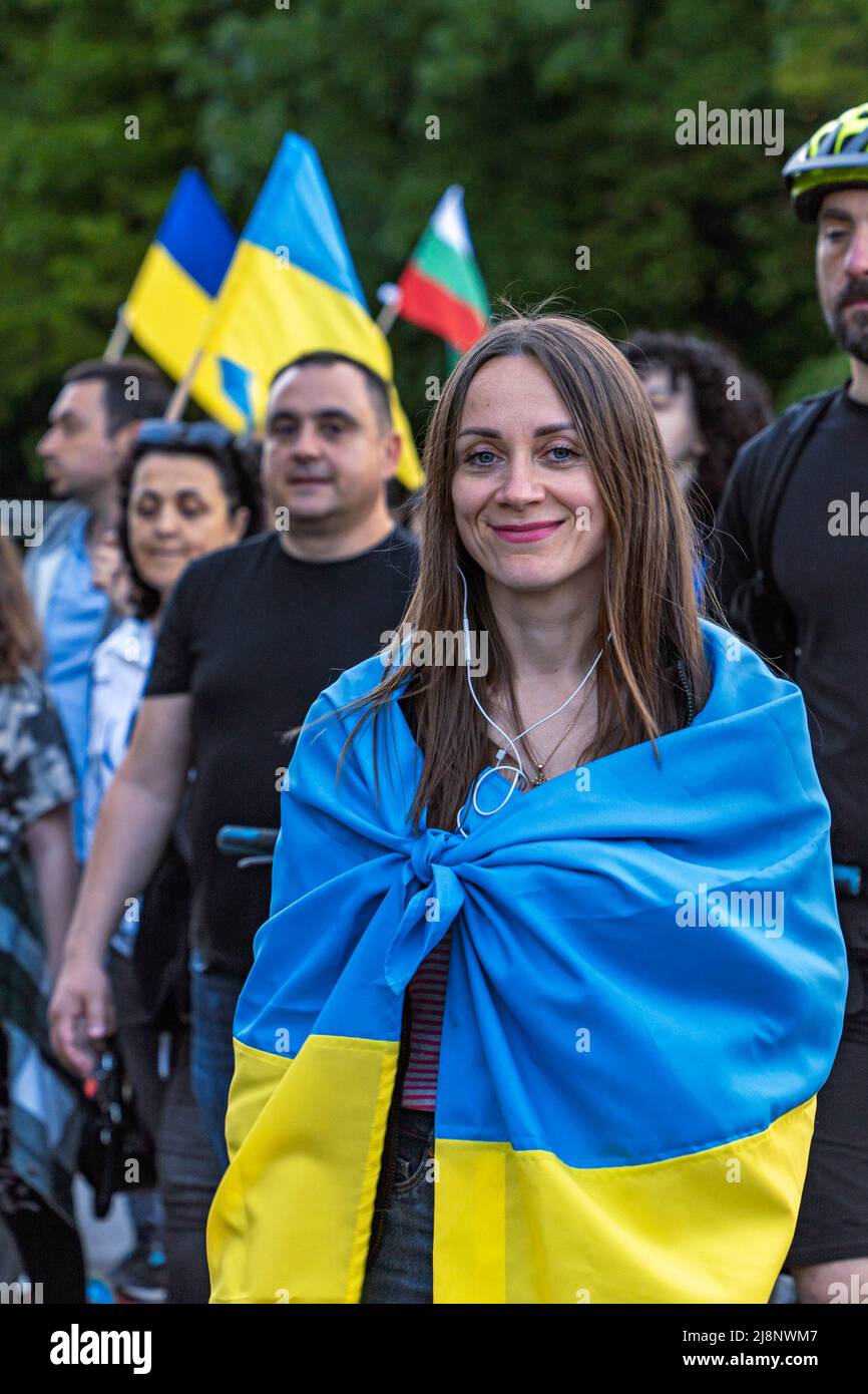 Sofia, Bulgarie - 09 mai 2022 : une jeune fille souriante, enveloppée d'un drapeau ukrainien, marche dans une foule à la manifestation de support Ukraine Banque D'Images