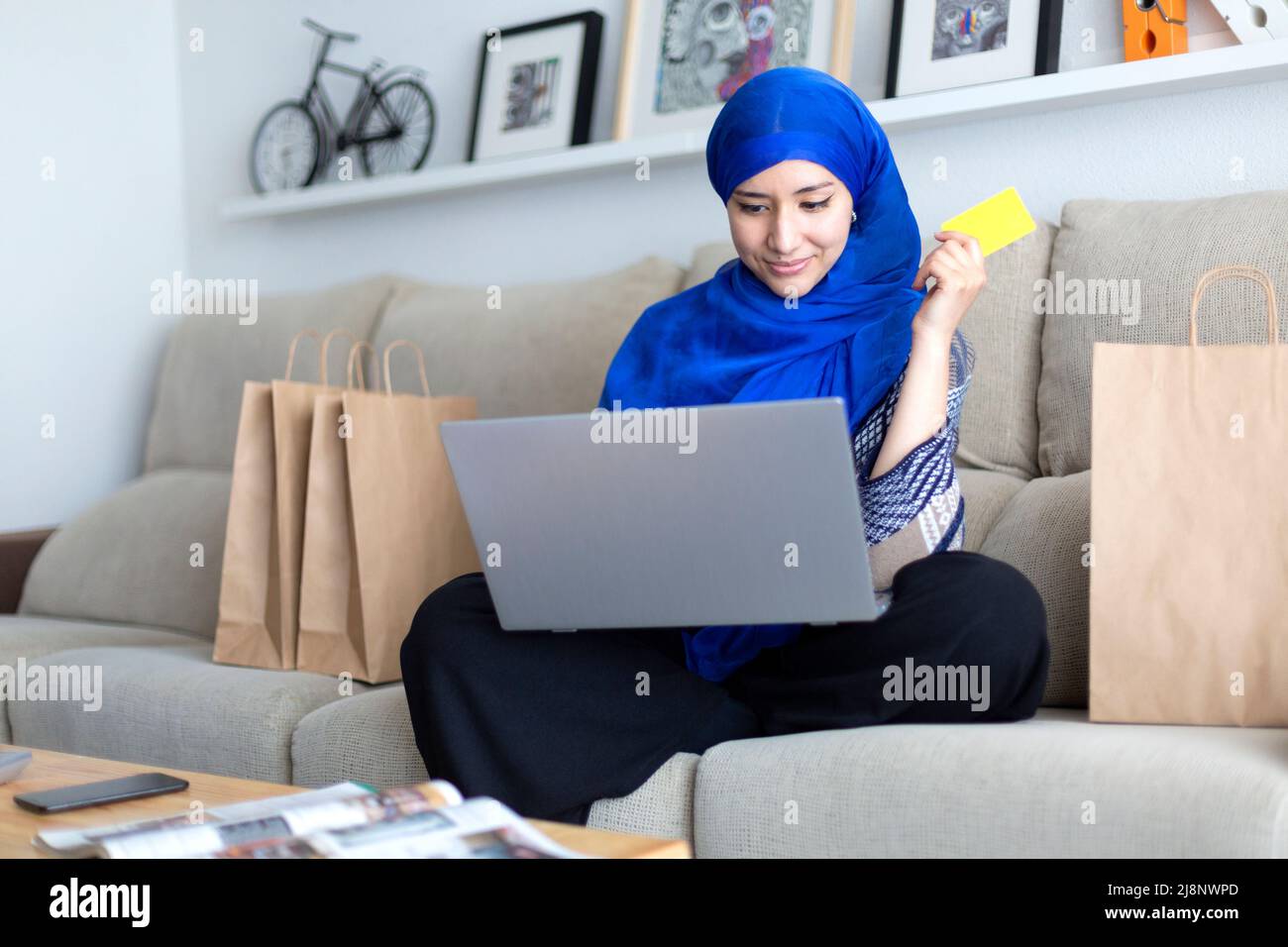 Jeune femme musulmane magasiner en ligne à la maison avec une carte de crédit et un ordinateur portable. Banque D'Images