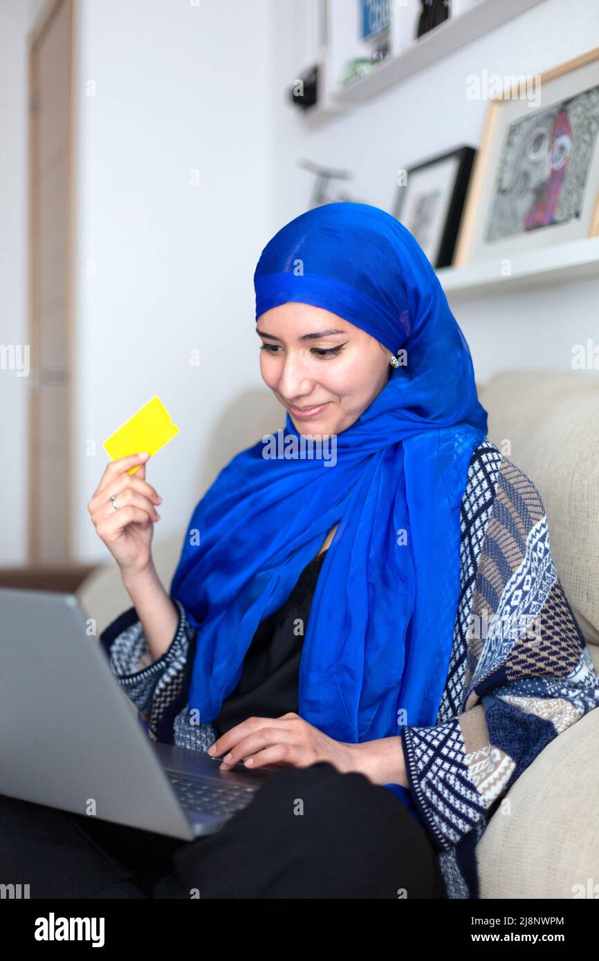 Jeune femme musulmane souriante magasiner en ligne à la maison avec une carte de crédit et un ordinateur portable. Banque D'Images