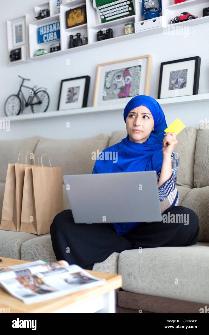 Une jeune femme musulmane choisit des produits à acheter chez elle. Achats en ligne avec carte de crédit. Banque D'Images