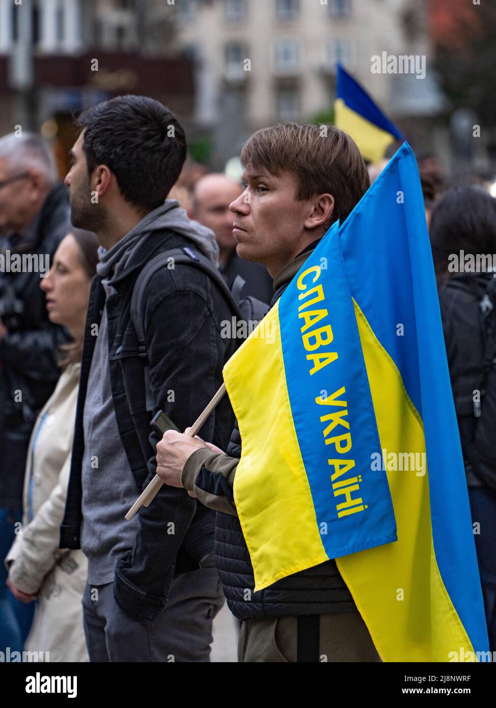 Un homme à la recherche concentrée se tient dans une foule avec le drapeau ukrainien avec le texte gloire à l'Ukraine Banque D'Images
