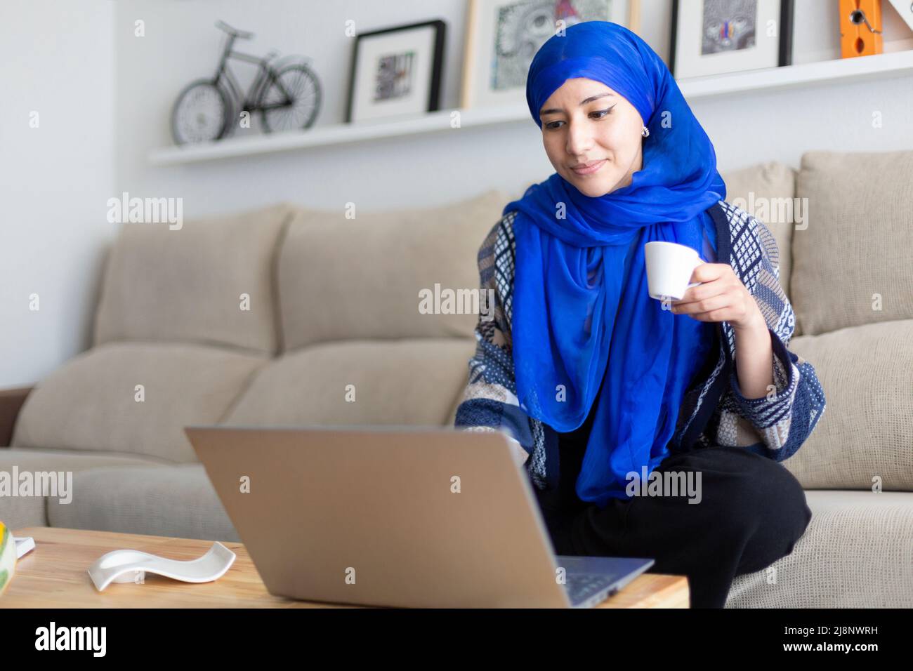 Jeune femme musulmane utilisant son ordinateur portable. Travailler à domicile, étudier en ligne, naviguer sur Internet. Espace pour le texte. Banque D'Images