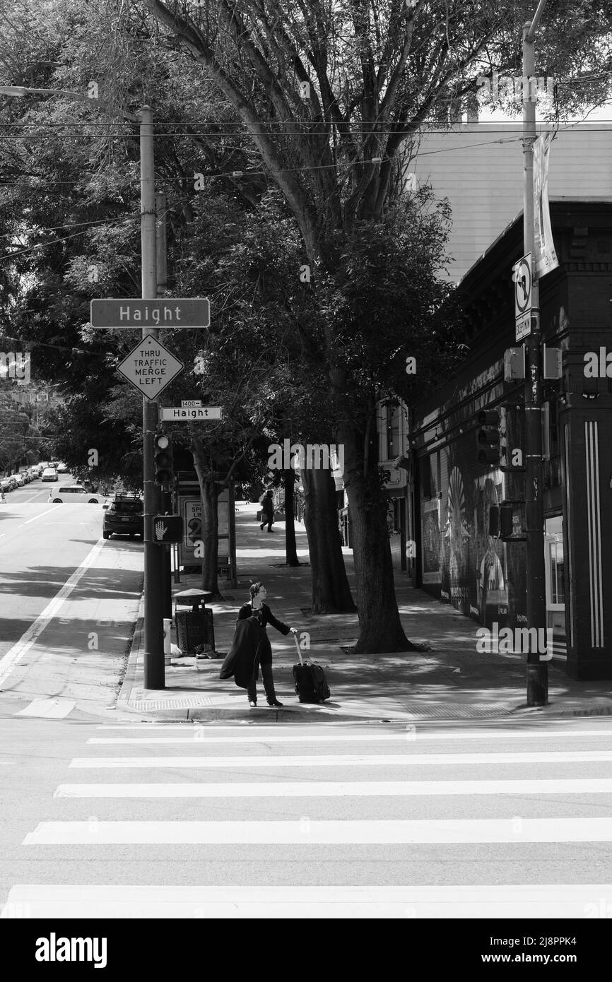 Jeune femme attendant de traverser la rue à l'angle de l'avenue Masonic et de la rue Haight; Haight-Ashbury District à San Francisco, Californie, valise. Banque D'Images