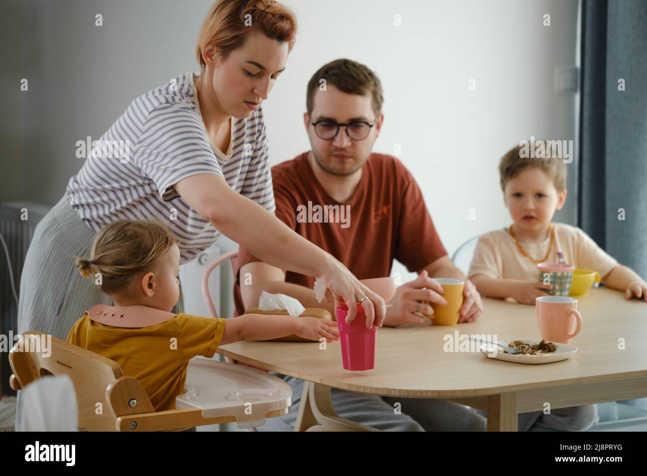 Parents avec enfants en repas, petit déjeuner à table. Mère servant de la nourriture à la famille à la maison. Manger avec les enfants. Fille en chaise haute manger Banque D'Images