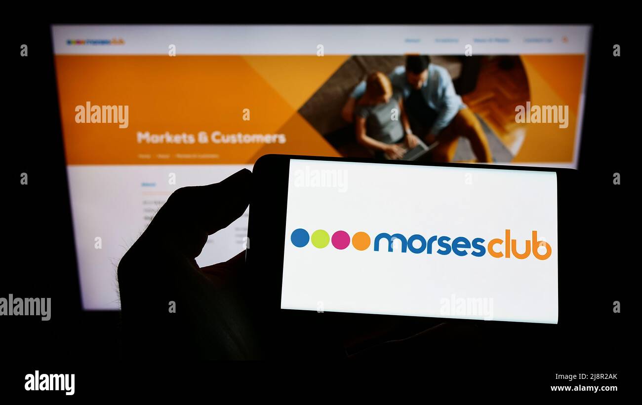 Personne tenant un téléphone portable avec le logo de la société financière britannique Morses Club plc à l'écran en face de la page Web d'affaires. Mise au point sur l'affichage du téléphone. Banque D'Images