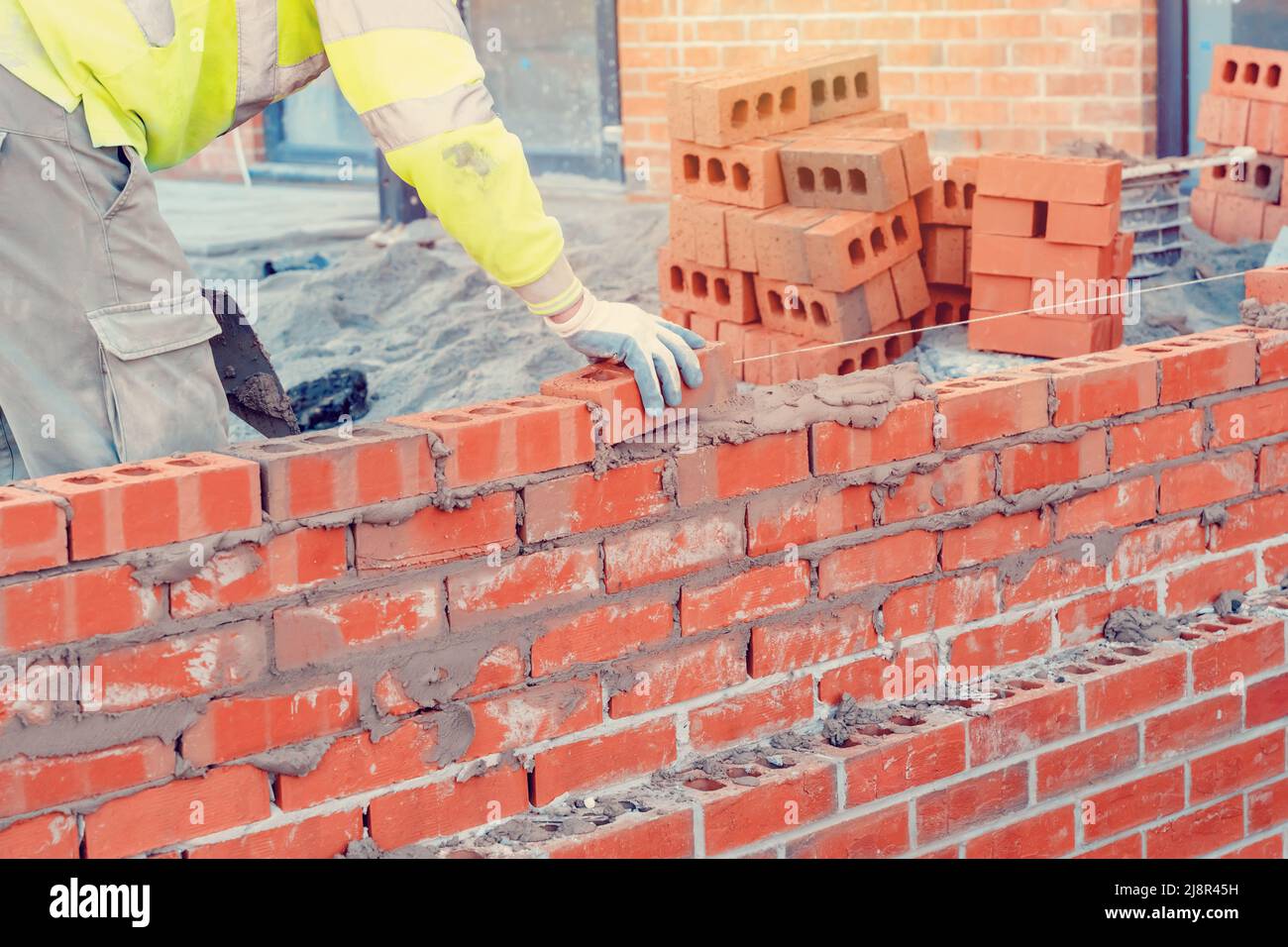 Bricklayer dans un gilet de sécurité et un casque posant un mur de briques à l'aide d'une truelle Banque D'Images