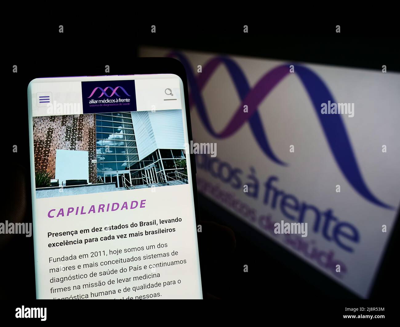 Personne tenant un téléphone portable avec le site Web de la société brésilienne de soins de santé Grupo Alliar à l'écran devant le logo. Concentrez-vous sur le centre de l'écran du téléphone. Banque D'Images