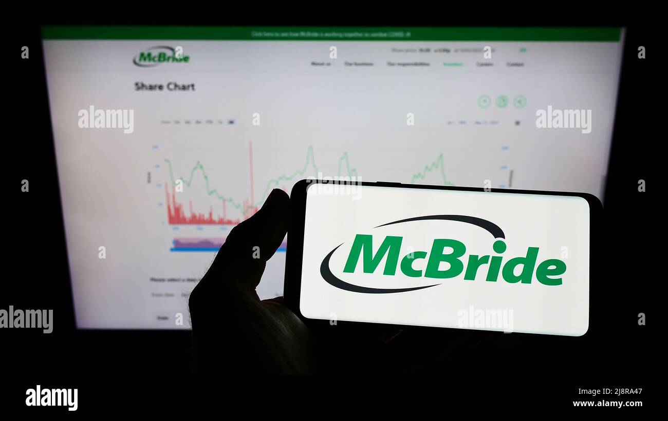 Personne tenant un smartphone avec le logo de la société britannique d'articles ménagers McBride plc à l'écran devant la page Web d'affaires. Mise au point sur l'affichage du téléphone. Banque D'Images