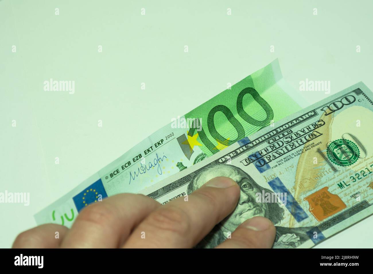 Deux billets sont pressés par les doigts de la main. 100 dollars et cent euros sur fond vert clair. Banque D'Images