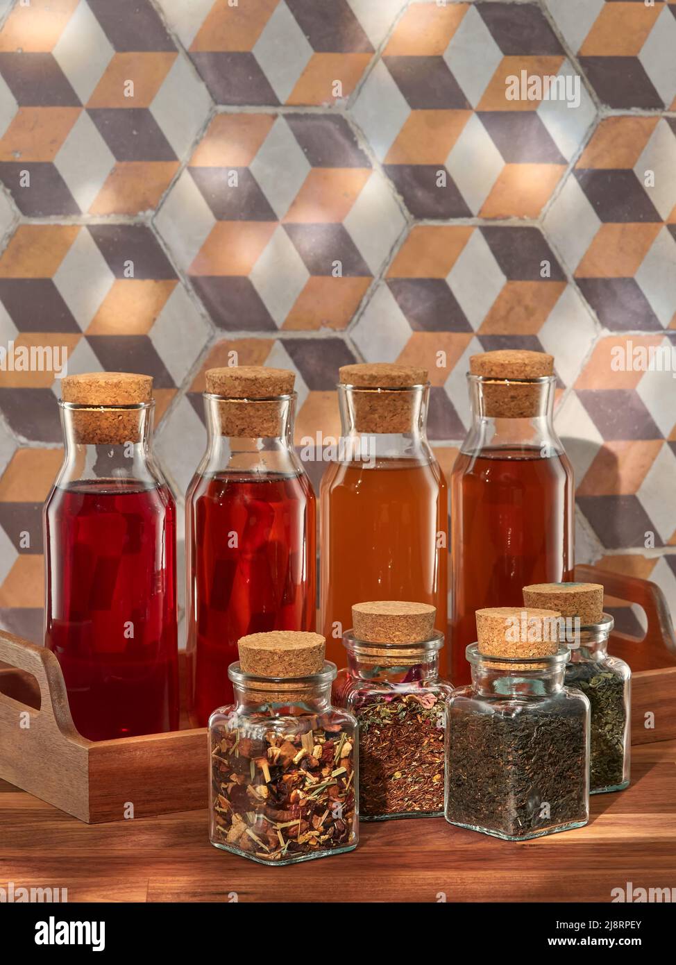 Quatre bouteilles de thé froid aux fruits, rooibos, vert et noir, avec quatre pots de thés séchés, dans un plateau en bois sur une table en bois Banque D'Images