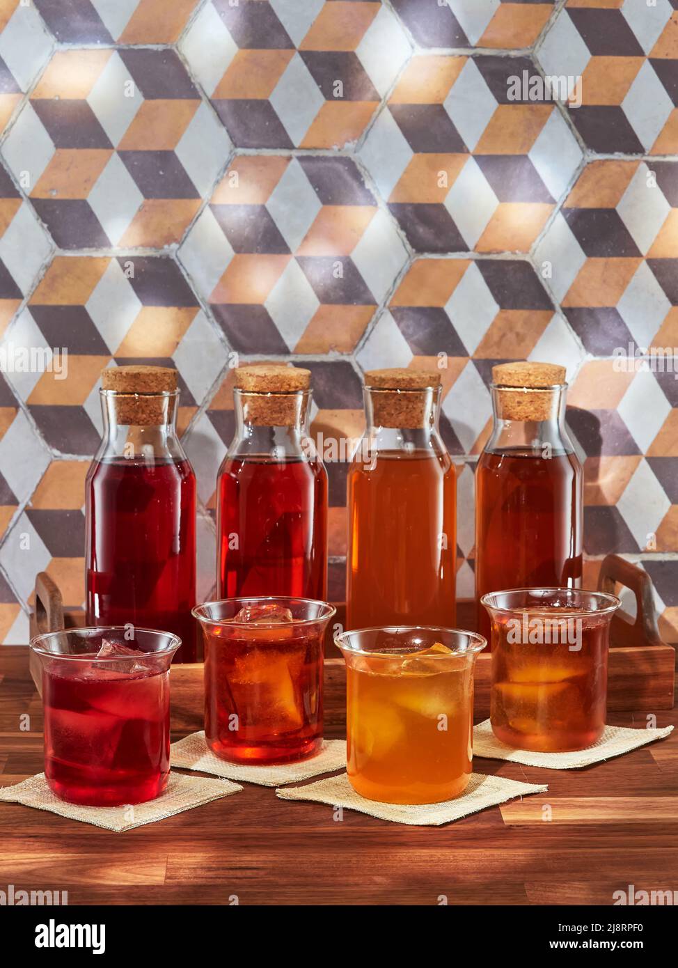 Quatre bouteilles et quatre verres de thé aux fruits, rooibos, vert et noir, dans un plateau en bois sur une table en bois Banque D'Images
