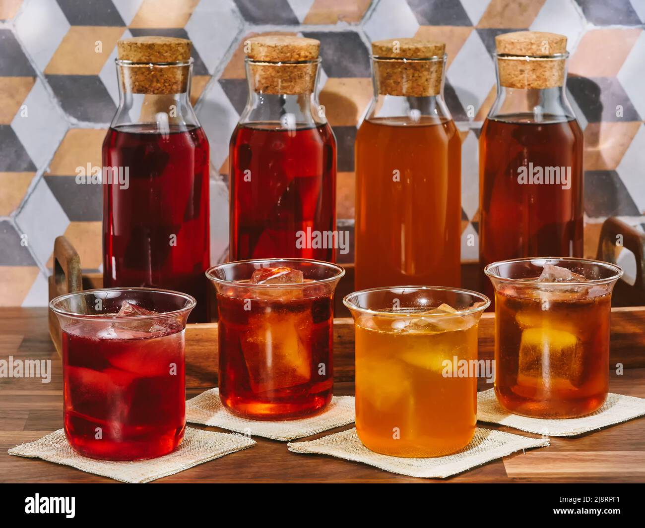 Quatre bouteilles et quatre verres de thé aux fruits, rooibos, vert et noir, dans un plateau en bois sur une table en bois Banque D'Images