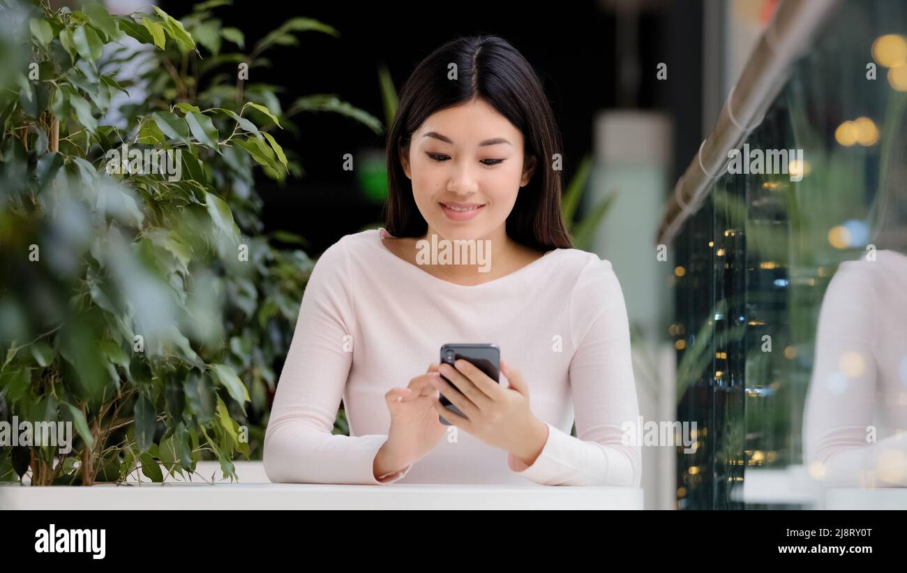 Asian Korean girl utilisateur indépendant joueur femme assis dans le café à la table au bureau avec le téléphone se réjouir célébrant la victoire gagner mobile jeu succ Banque D'Images