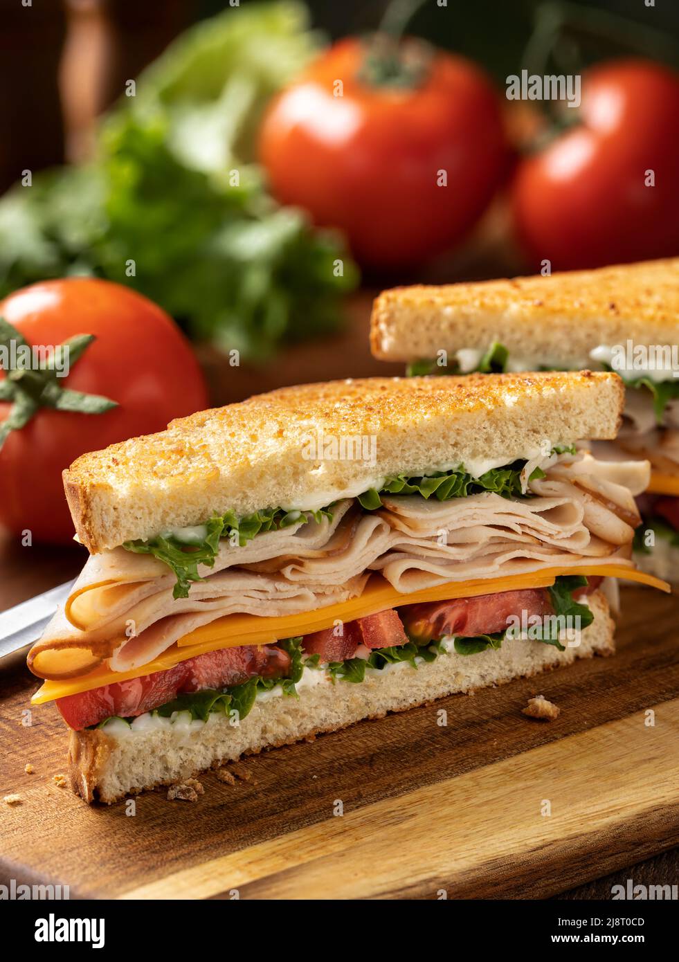 Sandwich à la dinde tranchée, au fromage, à la laitue et à la tomate sur du pain grillé coupé en deux sur une planche à découper Banque D'Images