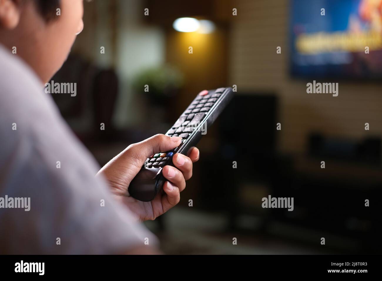 un adolescent tenant la télécommande de la télé dans un canapé Banque D'Images