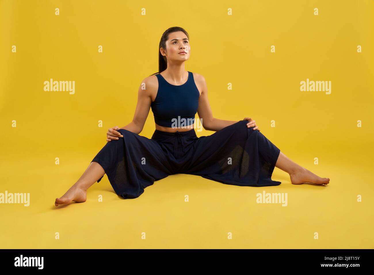 Jeune femme yogi faisant de l'exercice, étirant les jambes dans le studio spacieux. Femme caucasienne mince avec queue de cheval regardant vers le haut, tenant les bras à genoux écartés, isol Banque D'Images